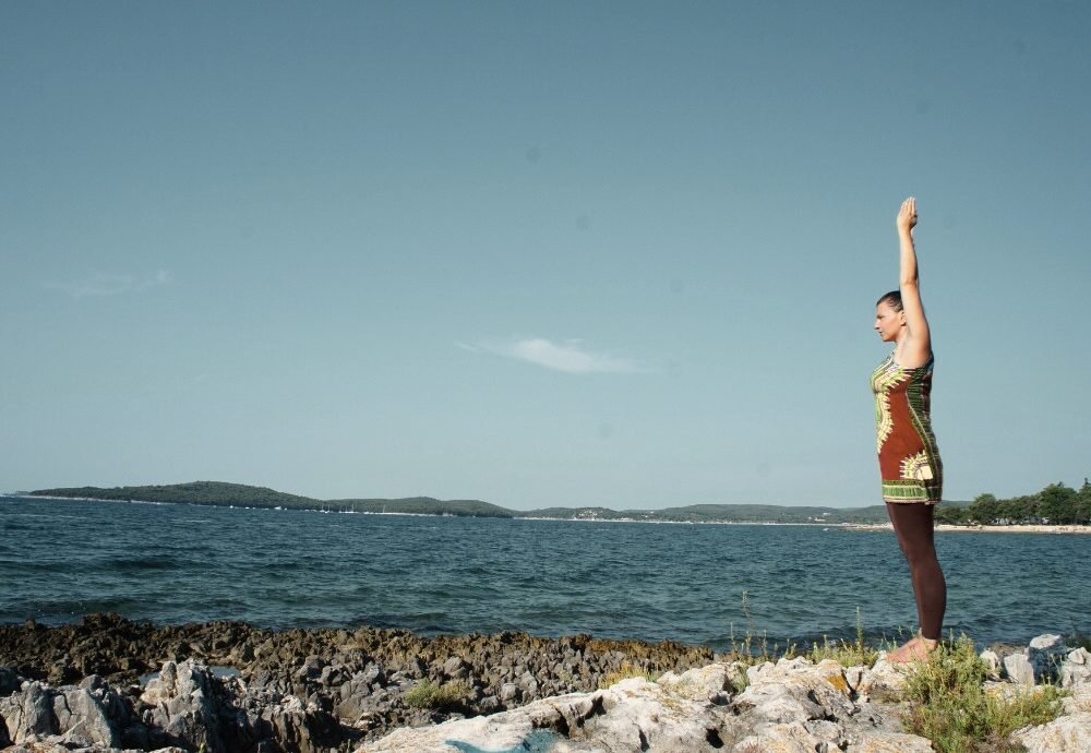 Manuela steht am Meer und streckt die Hände in die Höhe. Sie wirkt vollkommen in sich ruhend
