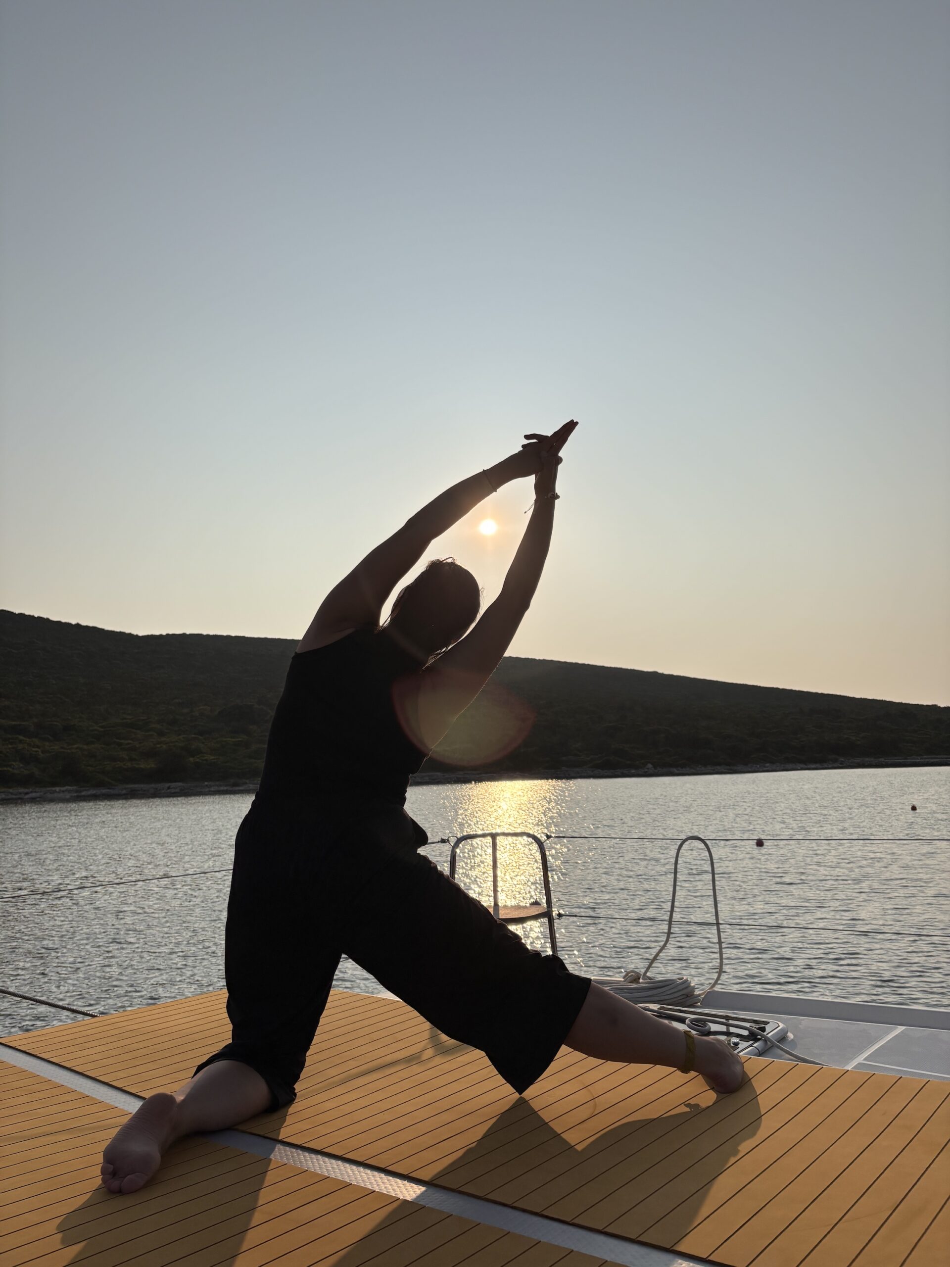 Manu in Yogapose "Torbogen" am Segelkatamaran mit Sonnenuntergangsstimmung